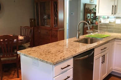 Exempel på ett avskilt, mellanstort klassiskt u-kök, med en undermonterad diskho, luckor med infälld panel, vita skåp, granitbänkskiva, grönt stänkskydd, stänkskydd i glaskakel, rostfria vitvaror, ljust trägolv, en halv köksö och brunt golv