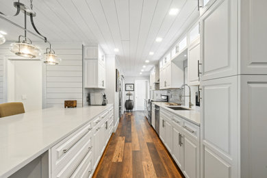 マイアミにある高級な中くらいなトランジショナルスタイルのおしゃれなキッチン (アンダーカウンターシンク、レイズドパネル扉のキャビネット、白いキャビネット、クオーツストーンカウンター、白いキッチンパネル、サブウェイタイルのキッチンパネル、シルバーの調理設備、クッションフロア、茶色い床、白いキッチンカウンター、塗装板張りの天井) の写真