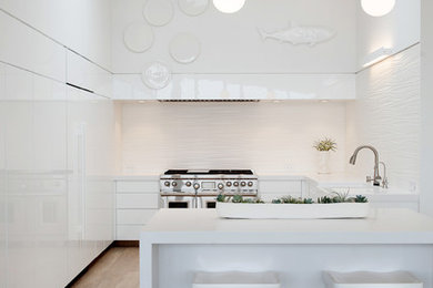 Example of a trendy u-shaped ceramic tile open concept kitchen design in San Francisco with a farmhouse sink, flat-panel cabinets, white cabinets, quartz countertops, white backsplash, ceramic backsplash, white appliances and an island
