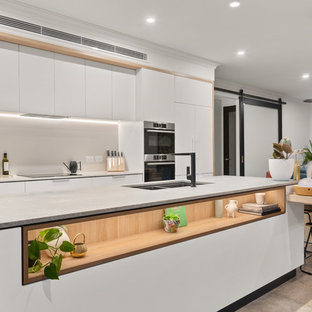 Design ideas for a contemporary open plan kitchen in Perth with a double-bowl sink, flat-panel cabinets, white cabinets, grey splashback, stainless steel appliances, with island, white benchtop and brown floor.