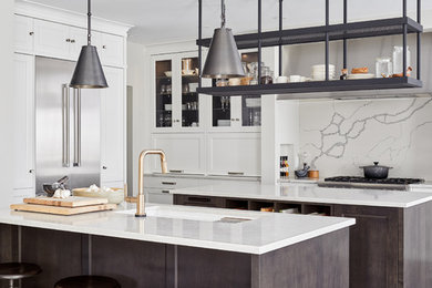 This is an example of a large country open plan kitchen in Ottawa with a submerged sink, recessed-panel cabinets, white cabinets, engineered stone countertops, white splashback, stone slab splashback, stainless steel appliances, dark hardwood flooring, multiple islands, brown floors and white worktops.
