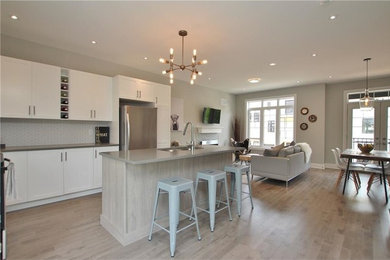 Inspiration for a mid-sized transitional l-shaped light wood floor and beige floor open concept kitchen remodel in Toronto with recessed-panel cabinets, white cabinets, solid surface countertops, an island, an undermount sink, white backsplash, glass tile backsplash and stainless steel appliances