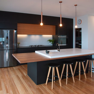 This is an example of a mid-sized contemporary galley open plan kitchen in Newcastle - Maitland with an undermount sink, flat-panel cabinets, black cabinets, concrete benchtops, white splashback, glass sheet splashback, stainless steel appliances, medium hardwood floors, with island, brown floor and grey benchtop.