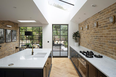 Eat-in kitchen - eclectic galley light wood floor and brown floor eat-in kitchen idea in London with a drop-in sink, recessed-panel cabinets, black cabinets, marble countertops, brick backsplash, black appliances, an island and white countertops