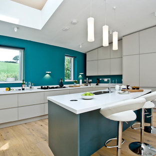 This is an example of a contemporary u-shaped kitchen in Devon with a double-bowl sink, flat-panel cabinets, white cabinets, blue splashback, light hardwood flooring, a breakfast bar, beige floors and white worktops.
