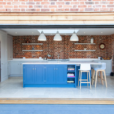 Example of a transitional u-shaped white floor enclosed kitchen design in Essex with shaker cabinets, blue cabinets, brick backsplash, stainless steel appliances, an island and white countertops
