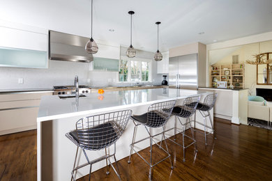 Modern inredning av ett kök, med släta luckor, vita skåp, bänkskiva i rostfritt stål, grått stänkskydd, rostfria vitvaror och en köksö