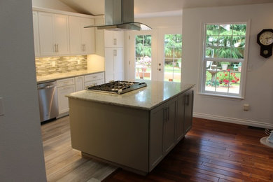 Foto på ett mellanstort funkis kök, med en undermonterad diskho, skåp i shakerstil, vita skåp, granitbänkskiva, stänkskydd i stickkakel, rostfria vitvaror, vinylgolv och en köksö