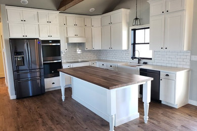 Eat-in kitchen - mid-sized cottage l-shaped vinyl floor and gray floor eat-in kitchen idea in Minneapolis with a farmhouse sink, flat-panel cabinets, white cabinets, quartz countertops, white backsplash, subway tile backsplash, stainless steel appliances, an island and white countertops