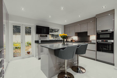 Design ideas for a medium sized contemporary u-shaped enclosed kitchen in Surrey with a single-bowl sink, flat-panel cabinets, grey cabinets, quartz worktops, black appliances, an island and grey worktops.