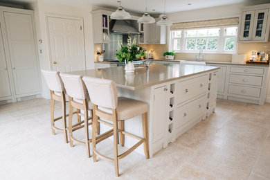 This is an example of a medium sized traditional l-shaped enclosed kitchen in West Midlands with a belfast sink, shaker cabinets, beige cabinets, an island and beige floors.
