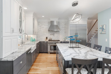 Example of a large transitional l-shaped light wood floor and brown floor eat-in kitchen design in Other with a farmhouse sink, raised-panel cabinets, gray cabinets, granite countertops, white backsplash, marble backsplash, stainless steel appliances and an island