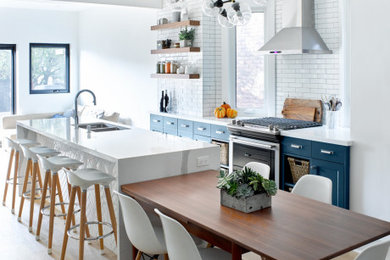 トロントにある広いトランジショナルスタイルのおしゃれなキッチン (ダブルシンク、シェーカースタイル扉のキャビネット、青いキャビネット、クオーツストーンカウンター、白いキッチンパネル、サブウェイタイルのキッチンパネル、シルバーの調理設備、淡色無垢フローリング、茶色い床、白いキッチンカウンター) の写真