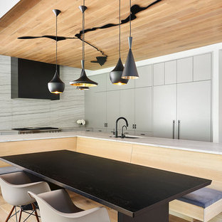 Immagine di una cucina design con lavello sottopiano, ante lisce, ante grigie, paraspruzzi bianco, elettrodomestici da incasso, parquet chiaro, isola, pavimento marrone e top bianco
