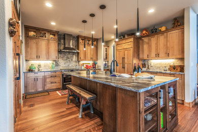 Inspiration for a large medium tone wood floor eat-in kitchen remodel in Denver with an undermount sink, recessed-panel cabinets, medium tone wood cabinets, granite countertops, multicolored backsplash, travertine backsplash, stainless steel appliances, an island and black countertops