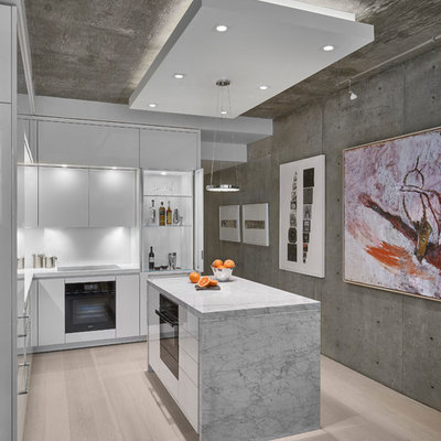Small trendy l-shaped light wood floor and beige floor kitchen photo in Chicago with white cabinets, white backsplash, an island, flat-panel cabinets, black appliances and white countertops