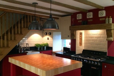 Large classic enclosed kitchen in Other with a belfast sink, beaded cabinets, red cabinets, granite worktops, ceramic splashback, black appliances, limestone flooring and an island.