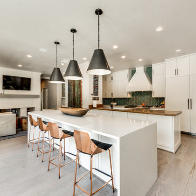 Example of a trendy single-wall light wood floor and brown floor open concept kitchen design in Dallas with a double-bowl sink, shaker cabinets, white cabinets, solid surface countertops, green backsplash, ceramic backsplash, stainless steel appliances and two islands