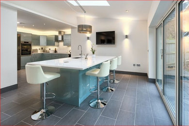 Inspiration for a medium sized contemporary l-shaped kitchen/diner in Cambridgeshire with flat-panel cabinets, stainless steel appliances, ceramic flooring, an island, blue cabinets, a built-in sink, white splashback and matchstick tiled splashback.