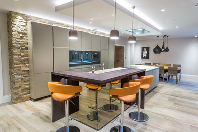 Contemporary galley kitchen/diner in Manchester with flat-panel cabinets, grey cabinets, wood worktops, black appliances, light hardwood flooring, an island, beige floors and white worktops.