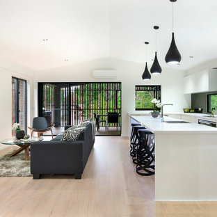 Design ideas for a contemporary galley open plan kitchen in Brisbane with an undermount sink, flat-panel cabinets, white cabinets, window splashback, black appliances, light hardwood floors, with island, beige floor and white benchtop.