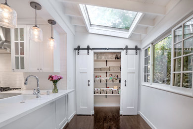 Mid-sized cottage u-shaped dark wood floor and brown floor enclosed kitchen photo in Los Angeles with a farmhouse sink, shaker cabinets, white cabinets, quartz countertops, white backsplash, porcelain backsplash, stainless steel appliances and a peninsula