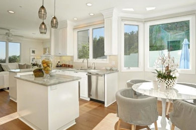 Open concept kitchen - mid-sized modern l-shaped light wood floor open concept kitchen idea in Los Angeles with an undermount sink, raised-panel cabinets, white cabinets, marble countertops, white backsplash, subway tile backsplash, stainless steel appliances and an island