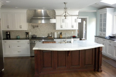 Inspiration for a mid-sized timeless u-shaped medium tone wood floor eat-in kitchen remodel in New York with a farmhouse sink, flat-panel cabinets, white cabinets, marble countertops, gray backsplash, glass tile backsplash, white appliances and an island