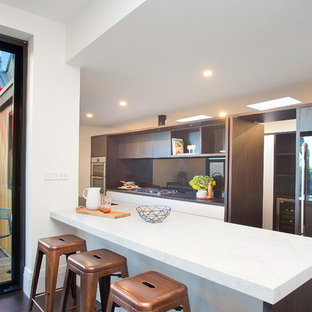 Inspiration for a contemporary single-wall separate kitchen in Sydney with flat-panel cabinets, brown cabinets, solid surface benchtops, mirror splashback, stainless steel appliances, with island, white benchtop, metallic splashback and brown floor.