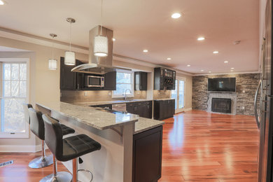 Kitchen - large transitional l-shaped medium tone wood floor and brown floor kitchen idea in Baltimore with an undermount sink, raised-panel cabinets, dark wood cabinets, granite countertops, beige backsplash, ceramic backsplash, stainless steel appliances and a peninsula