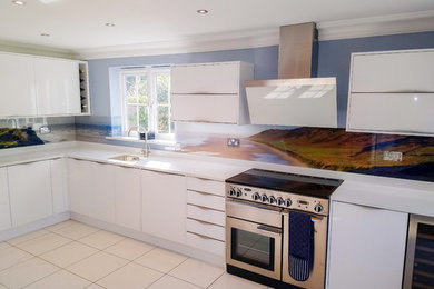 Medium sized beach style l-shaped kitchen in Sussex with an integrated sink, flat-panel cabinets, white cabinets, multi-coloured splashback, stainless steel appliances, ceramic flooring, no island, beige floors and white worktops.