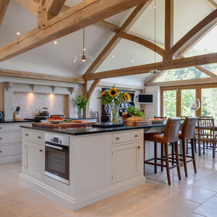 This is an example of a large rural single-wall kitchen in Other with recessed-panel cabinets, grey cabinets, beige splashback, stainless steel appliances, an island, beige floors and black worktops.