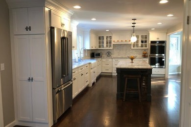 Large transitional l-shaped dark wood floor and brown floor eat-in kitchen photo in Boston with a farmhouse sink, shaker cabinets, white cabinets, granite countertops, gray backsplash, porcelain backsplash, stainless steel appliances, an island and gray countertops