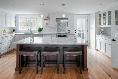 Example of a large transitional l-shaped medium tone wood floor and brown floor enclosed kitchen design in Boston with an undermount sink, shaker cabinets, white cabinets, marble countertops, white backsplash, subway tile backsplash, stainless steel appliances and an island
