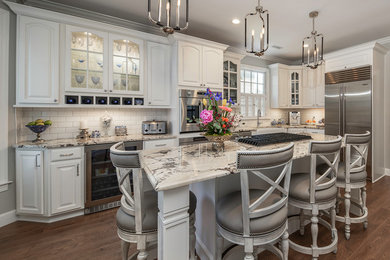 Inspiration for a timeless l-shaped dark wood floor and brown floor eat-in kitchen remodel in Other with a farmhouse sink, raised-panel cabinets, white cabinets, granite countertops, subway tile backsplash, stainless steel appliances, an island, white backsplash and gray countertops