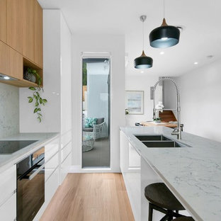 Photo of a contemporary galley separate kitchen in Brisbane with an undermount sink, flat-panel cabinets, medium wood cabinets, grey splashback, black appliances, light hardwood floors, with island, beige floor and grey benchtop.