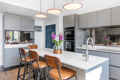 Inspiration for a medium sized contemporary l-shaped kitchen/diner in Other with a submerged sink, flat-panel cabinets, grey cabinets, multi-coloured splashback, mirror splashback, black appliances, slate flooring, an island and brown floors.