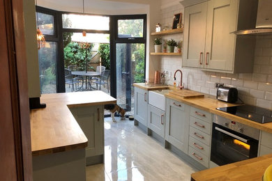 Photo of a small modern l-shaped enclosed kitchen in Other with a belfast sink, shaker cabinets, grey cabinets, wood worktops, ceramic flooring, a breakfast bar and beige floors.