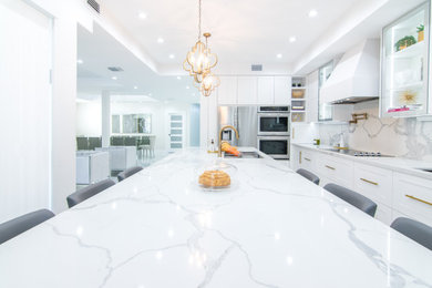Example of a large transitional l-shaped porcelain tile and white floor open concept kitchen design in Miami with shaker cabinets, white cabinets, quartz countertops, an island, white countertops, an undermount sink, white backsplash, porcelain backsplash and stainless steel appliances