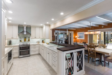 Inspiration for a mid-sized transitional u-shaped ceramic tile eat-in kitchen remodel in Tampa with a single-bowl sink, raised-panel cabinets, white cabinets, solid surface countertops, blue backsplash, porcelain backsplash, stainless steel appliances and an island