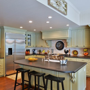 Large traditional open concept kitchen appliance - Example of a large classic l-shaped open concept kitchen design in Houston with an undermount sink, raised-panel cabinets, green cabinets, granite countertops, beige backsplash, stone tile backsplash, stainless steel appliances and an island