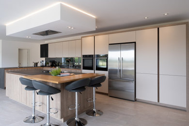 Modern inredning av ett stort grå grått kök, med släta luckor, vita skåp, grått stänkskydd, glaspanel som stänkskydd, klinkergolv i porslin, en köksö och flerfärgat golv