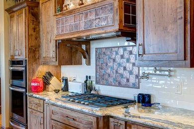 Mid-sized mountain style single-wall light wood floor and brown floor enclosed kitchen photo in Other with recessed-panel cabinets, dark wood cabinets, granite countertops, white backsplash, stone tile backsplash, stainless steel appliances and an island
