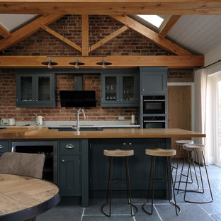 Medium sized rustic l-shaped open plan kitchen in Cheshire with shaker cabinets, brick splashback, stainless steel appliances, an island and black floors.