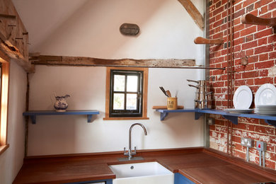 Ejemplo de cocinas en L de estilo de casa de campo pequeña cerrada sin isla con fregadero sobremueble, puertas de armario azules, encimera de madera y suelo de baldosas de terracota