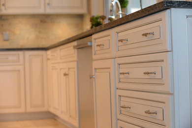 Example of a large classic porcelain tile kitchen design in Cleveland with white cabinets, raised-panel cabinets, stainless steel appliances, an island and stone tile backsplash
