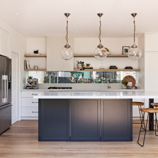 Photo of a beach style l-shaped kitchen in Newcastle - Maitland with an undermount sink, shaker cabinets, white cabinets, white splashback, stainless steel appliances, light hardwood floors, with island, beige floor and white benchtop.