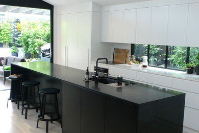 Bild på ett mellanstort funkis vit vitt kök, med en undermonterad diskho, släta luckor, svarta skåp, bänkskiva i koppar, vitt stänkskydd, glaspanel som stänkskydd, svarta vitvaror, målat trägolv, en köksö och vitt golv