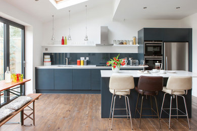 ロンドンにある高級な中くらいなコンテンポラリースタイルのおしゃれなキッチン (フラットパネル扉のキャビネット、グレーのキャビネット、人工大理石カウンター、グレーのキッチンパネル、ガラス板のキッチンパネル、一体型シンク、パネルと同色の調理設備、茶色い床、白いキッチンカウンター、折り上げ天井) の写真