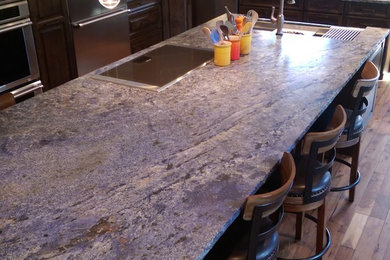 Example of a large mountain style l-shaped medium tone wood floor and brown floor eat-in kitchen design in Denver with an undermount sink, raised-panel cabinets, dark wood cabinets, granite countertops, beige backsplash, stone tile backsplash, stainless steel appliances and an island